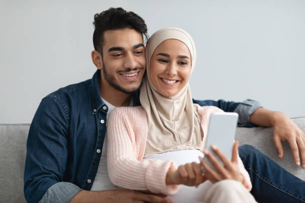 istock Cheerful Pregnant Middle Eastern Spouses Browsing Internet On Smartphone Together At Home 1322978395