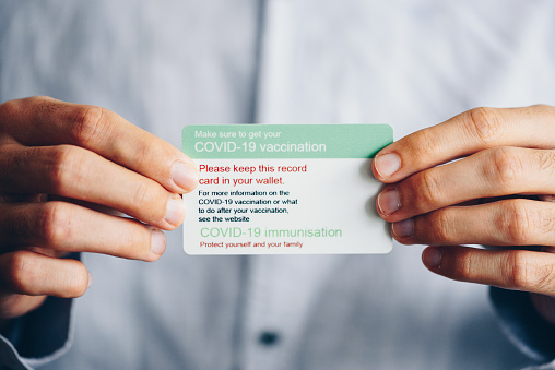 Unrecognizable man holding a vaccination card for Covid 19 immunization close up photo. Coronavirus pandemic concept. Vaccination ID card close up. (NOT real ID card)