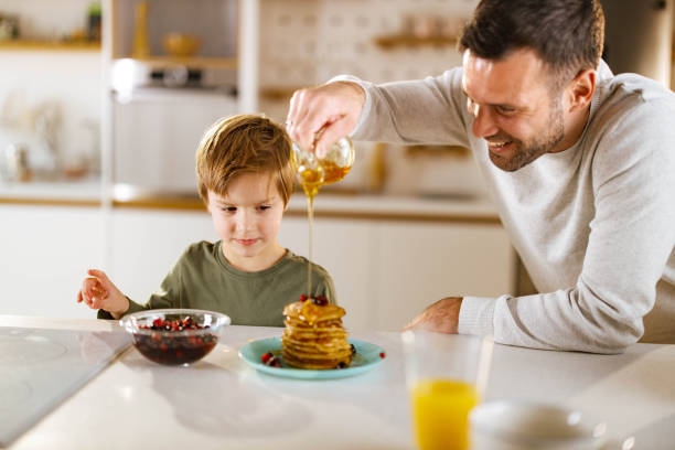 istock Happy single father decorating pancakes for his son at home. 1322980964