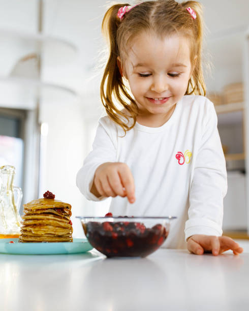 istock Happy girl decorating pancakes in dining room. 1322981092