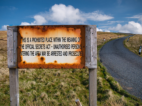 An old, rusting sign advises that the area ahead is a prohibited place under the UK's Official Secrets Act and that unauthorised entry may result in arrest and prosecution.