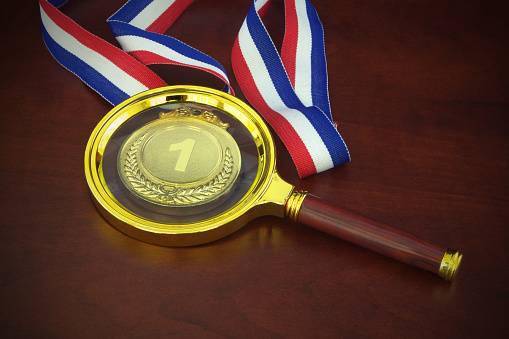 Investigate result of competition concept. Gold medal and magnifying glass.