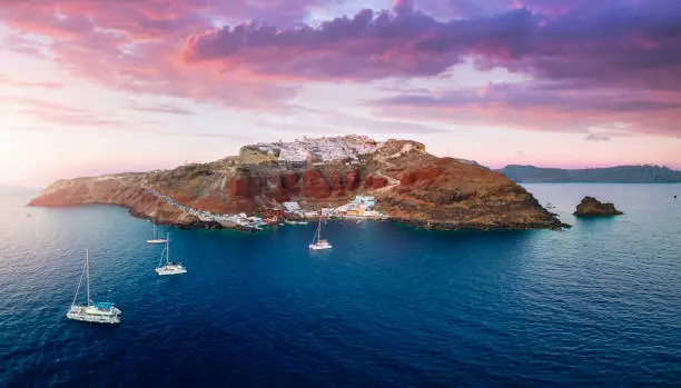 Panoramic aerial view to the villages of Oia and Ammoudi surrounded by the steep, volcanic rock formations on Santorini island, Greece, during summer sunset time