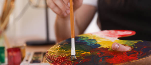 istock Young man with painting tools at table in artist studio, closeup. Banner design 1322995916