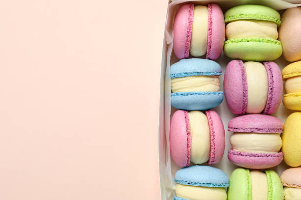 istock Many delicious colorful macarons in box on pink background, top view. Space for text 1322996370