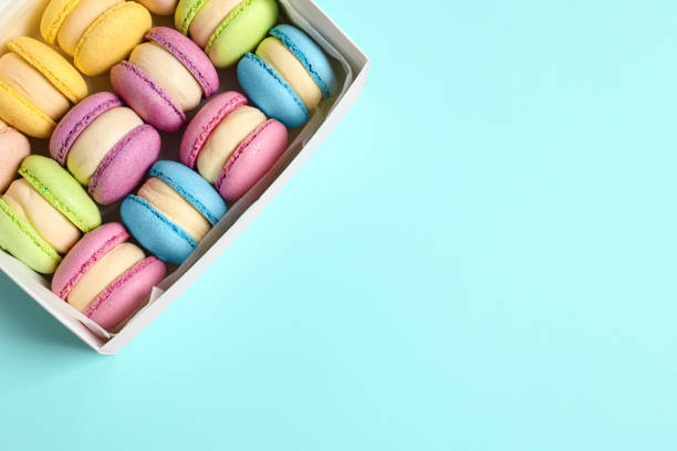 istock Many delicious colorful macarons in box on light blue background, top view. Space for text 1322996454