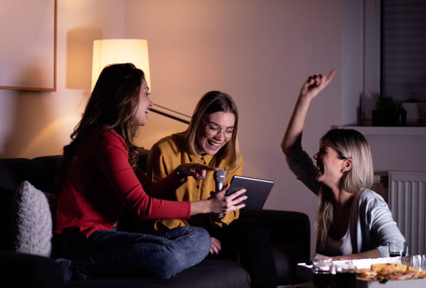 istock Three female friends having fun sitting on sofa playing karaoke at home. 1322997185