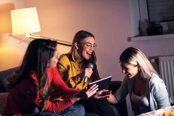 istock Three female friends having fun sitting on sofa playing karaoke at home. 1322997188