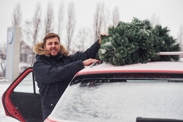 istock Young man standing near car with green christmas tree on top 1322997192