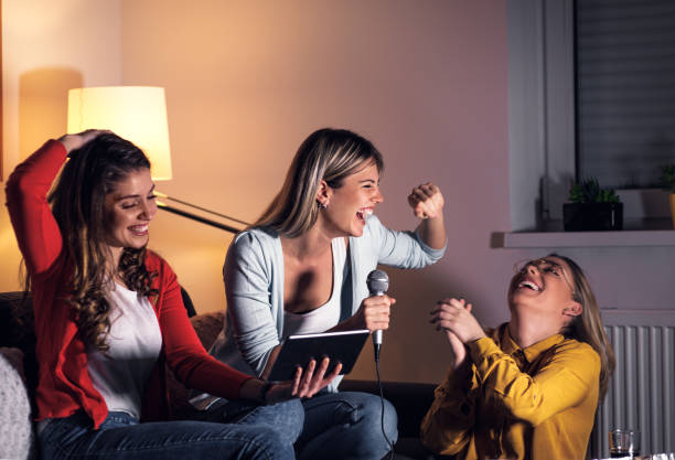 istock Three female friends having fun sitting on sofa playing karaoke at home. 1322997230