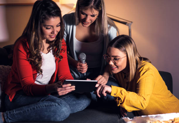 istock Three female friends having fun sitting on sofa playing karaoke at home. 1322997233