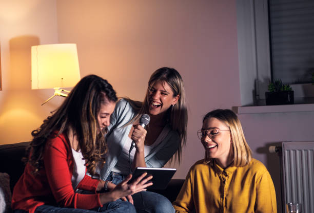 istock Three female friends having fun sitting on sofa playing karaoke at home. 1322997234