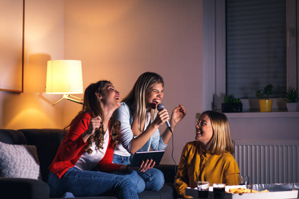 istock Three female friends having fun sitting on sofa playing karaoke at home. 1322997280