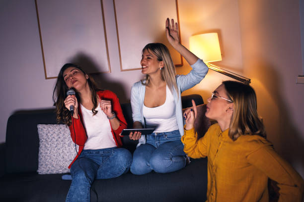 istock Three female friends having fun sitting on sofa playing karaoke at home. 1322997287