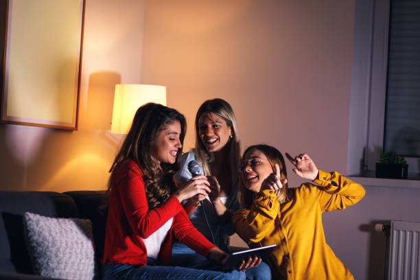 istock Three female friends having fun sitting on sofa playing karaoke at home. 1322997290