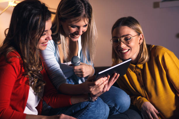 istock Three female friends having fun sitting on sofa playing karaoke at home. 1322997381
