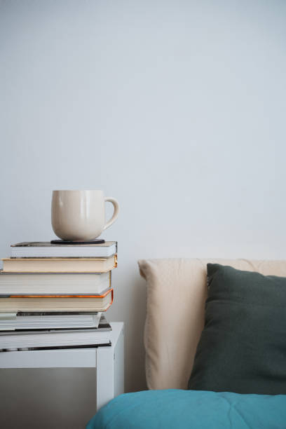 coffee cup tea mug on stack of books next to a bed. White background front view