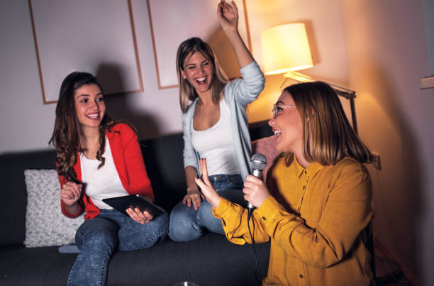 istock Three female friends having fun sitting on sofa playing karaoke at home. 1322997467