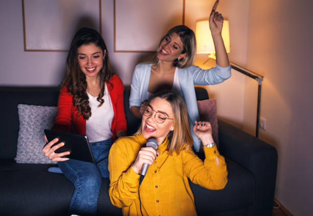 istock Three female friends having fun sitting on sofa playing karaoke at home. 1322997486