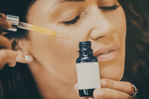 mujer aplicando suero facial. - vitamin c fotografías e imágenes de stock