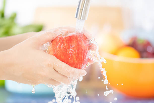 young woman washing a red apple under faucet in the sink kitchen