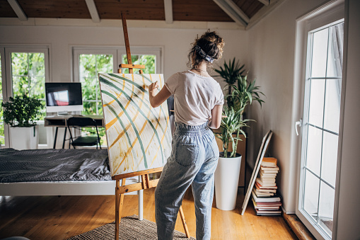 One woman, beautiful young female artist, painting on canvas in her home studio.