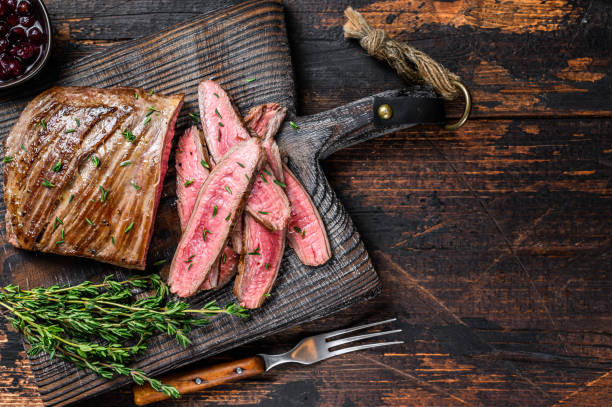 BBQ sliced skirt beef meat steak on a wooden cutting board. Dark wooden background. Top view. Copy space BBQ sliced skirt beef meat steak on a wooden cutting board. Dark wooden background. Top view. Copy space. flank steak stock pictures, royalty-free photos & images