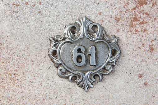 Old aluminum door number 61 on concrete background. Copy space for text.