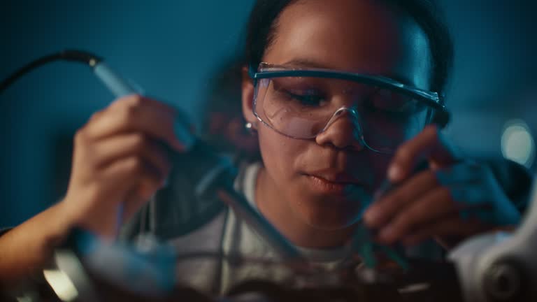 Young Teenage Multiethnic Schoolgirl is Studying Electronics and Soldering Wires and Circuit Boards in Her Science Hobby Robotics Project. Girl is Working on a Robot in Her Room. Education Concept.