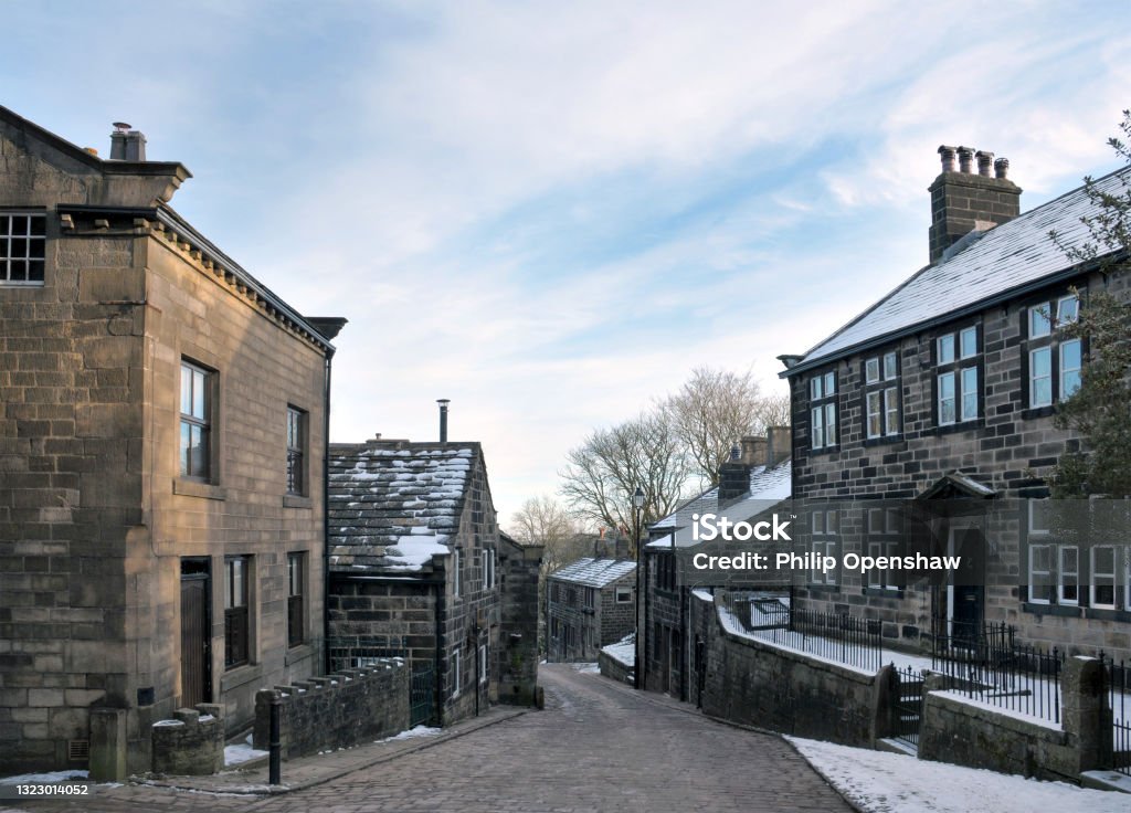 view of the main street in the village of Heptonstall in west Yorkshire with snow on roofs with blue winter sky Snow Stock Photo