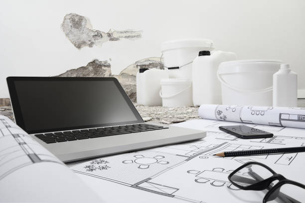 istock house renovation and plan concept. Computer, eyeglasses, and phone above the blue print project draw. Buckets and jerry can products for painting and plastering in wall background with copy space 1323016261