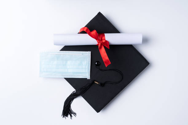 istock Graduation academic cap with diploma and mask isolated on white table background. 1323018578