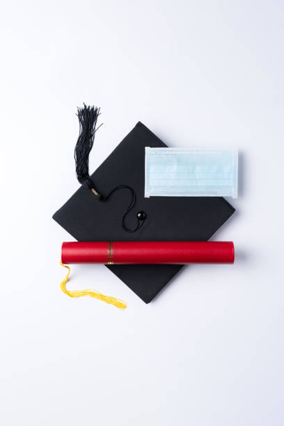 istock Graduation academic cap with diploma and mask isolated on white table background. 1323018600