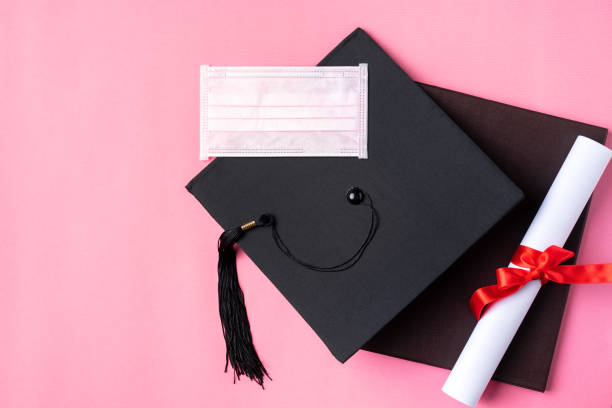 istock Graduation academic cap with diploma and mask isolated on pink table background. 1323018942