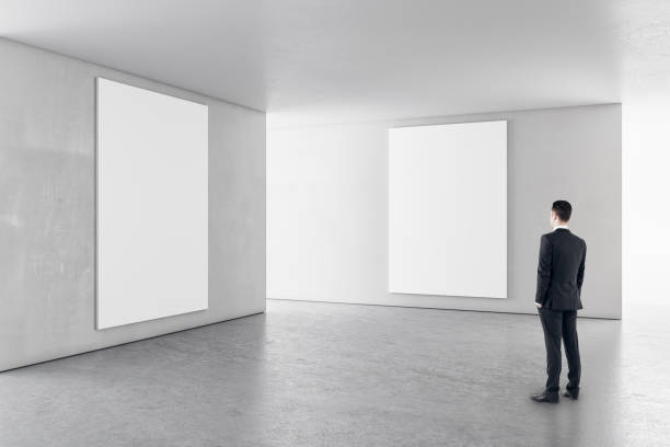 istock Businessman in contemporary concrete interior with empty banners looking at mockup place for your advertisement. 1323020192