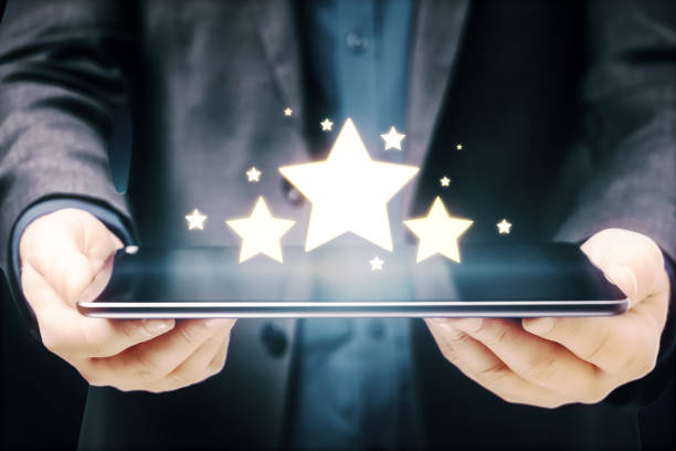 istock Businessman hands holding tablet with glowing stars on blue background. Customer feedback and online ranking concept. 1323020354