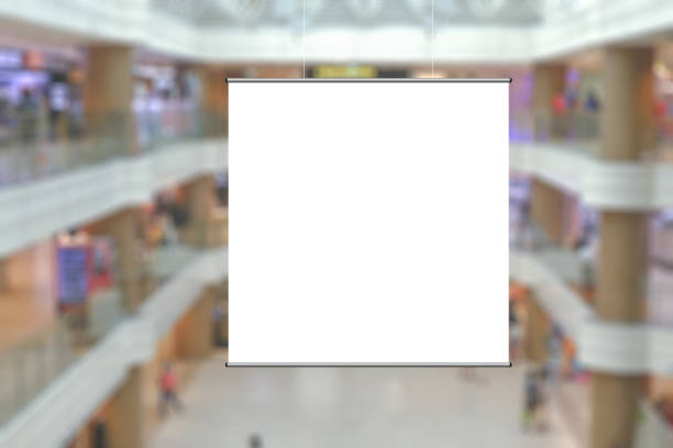 istock Blank advertising poster banner mockup in modern retail environment; square hanging billboard in shopping mall, out-of-home OOH media display space; blur background. 1323020491