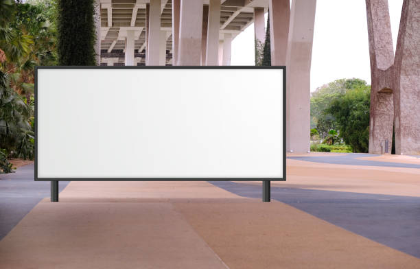 Blank large billboard advertising banner mockup in a large open space with plants under a modern bridge. Large horizontal digital display screen, an out-of-home OOH media display space.
