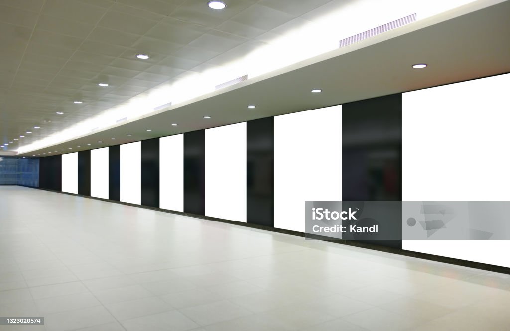 Multiple vertical blank white panels of advertising billboard poster templates in a long tunnel walkway; out-of-home OOH media display space mockup in pedestrian linkway; digital display. Multiple vertical blank white panels of advertising billboard poster templates in a long tunnel walkway; out-of-home OOH media display space mockup in pedestrian linkway; digital display Airport Stock Photo