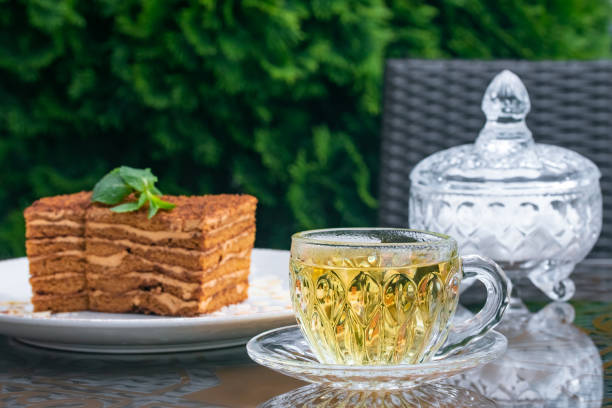 istock Crystal cup with mint tea, sugar bowl and medovik cake on table in summer cafe. Tea drinking concept, British culture. Still life. Lifestyle. Traditional Russian cuisine, dessert. 1323022558