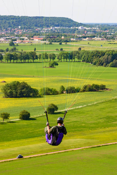 parapente sentado em um arreio e voando sobre uma paisagem rural - 5416 - fotografias e filmes do acervo