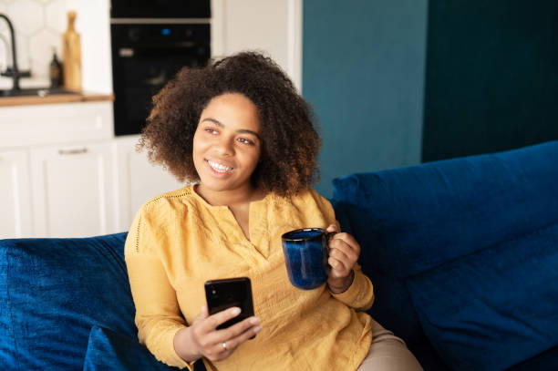 istock Woman sitting on the sofa with mug in hands, using smartphone 1323027548