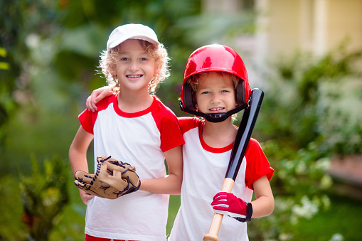 Kids play baseball. Child with bat and ball. Outdoor activity for healthy kids. Fun team ball game for boy and girl. Young athlete on baseball field. Little boy with helmet for safe exercise.