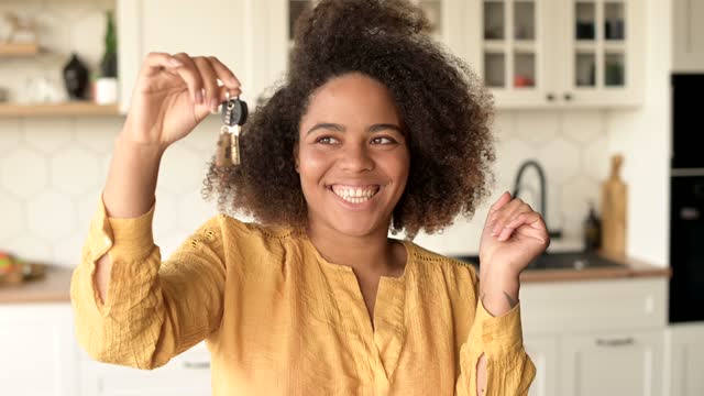 Overjoyed African-American woman holding keys in hand, buying own estate