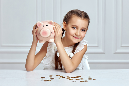 happy little child girl saving money for future in pink piggy bank