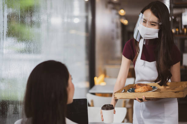 istock Asian waitress with face protective mask and face shield serving coffee and bread in coffee shop 1323034937