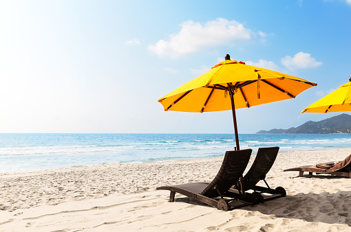 Beach chairs with yellow umbrella and beautiful sand beach in Koh Samui, Thailand. Vacation holidays summer background. View of nice tropical beach.