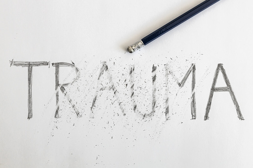 Borrando el trauma. Trauma escrito en papel blanco con un lápiz, parcialmente borrado con una goma de borrar. Simbólico para superar el trauma o tratar el trauma. photo