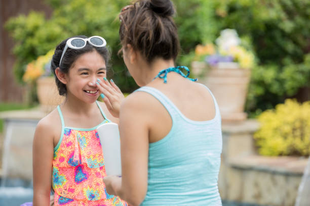 Young daughter smiling while her mother applies sunscreen to her nose Young daughter smiling while her mother applies sunscreen to her nose swimming protection stock pictures, royalty-free photos & images