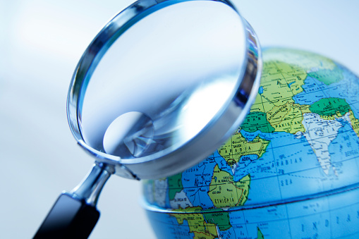 A magnifying glass in front of a globe that is rotated to show Africa and Asia. Photographed with a very shallow depth of field.